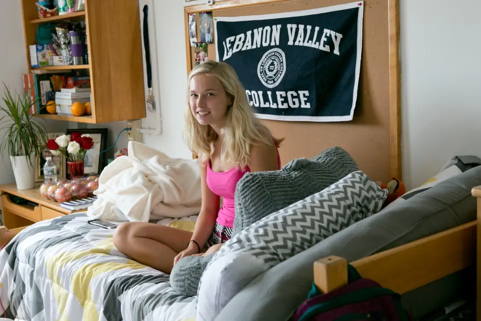 Student sitting on bed in dorm room