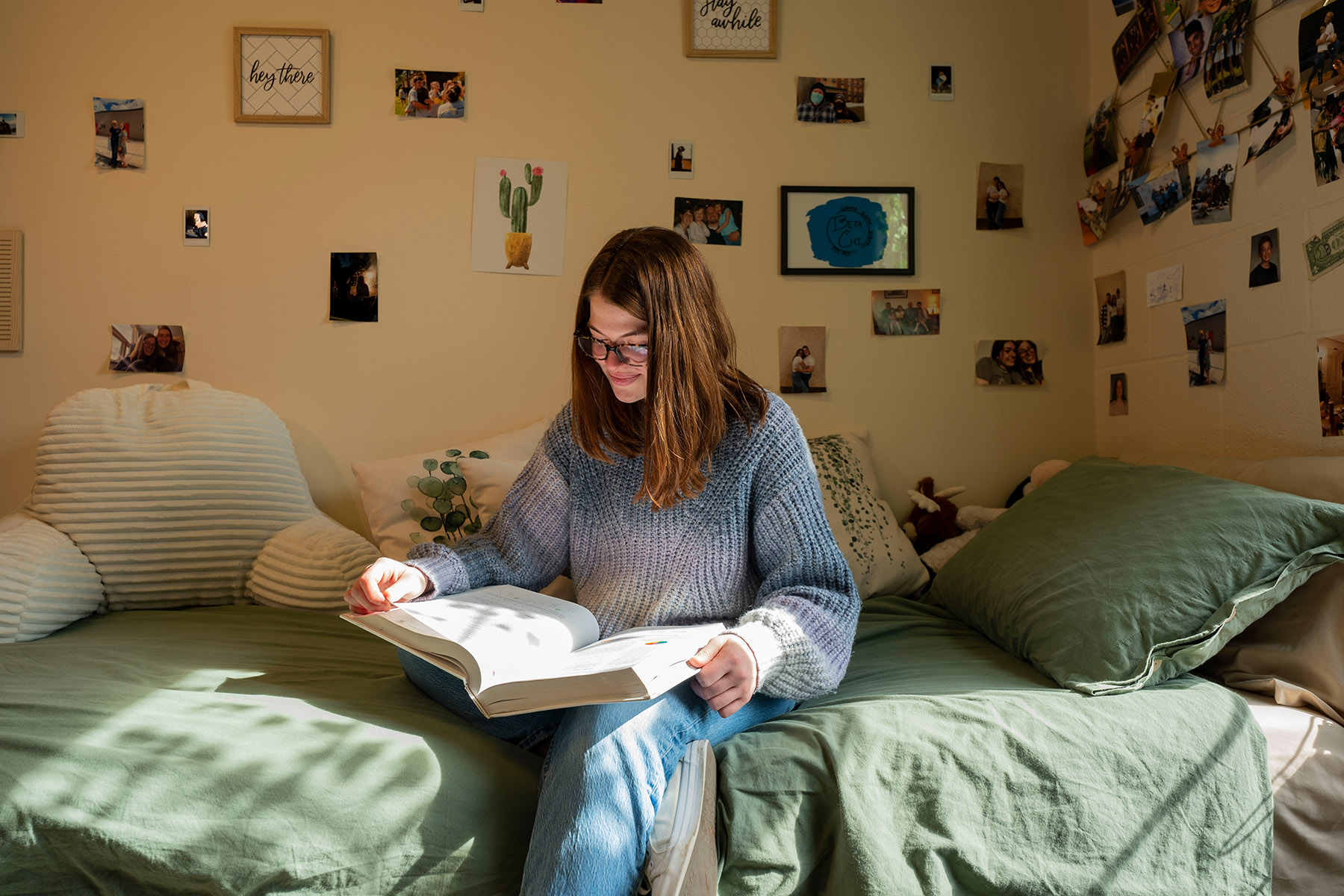 LVC student in light blue pullover sits on dorm room bed reading.