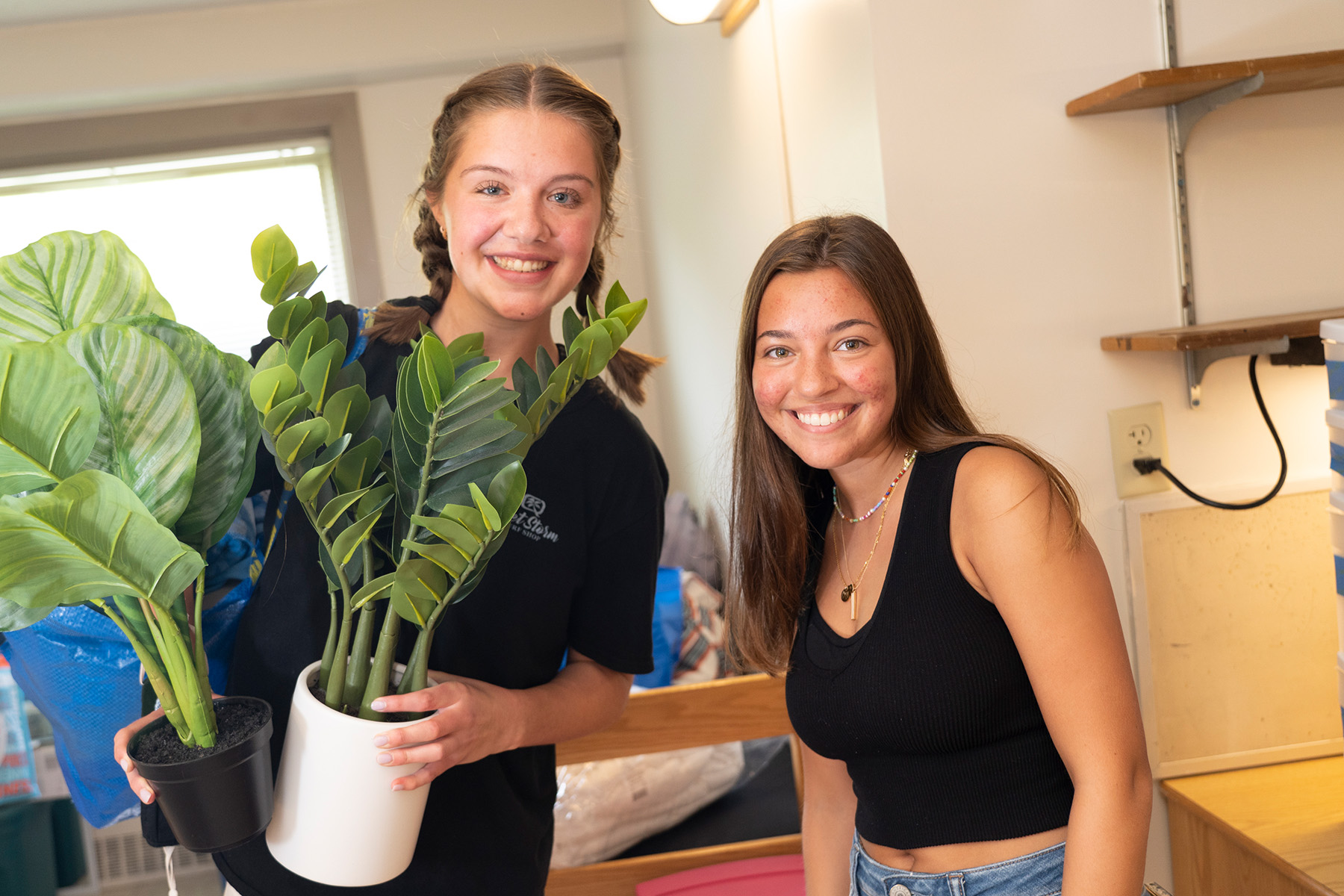 Two students smile while holding a plant.