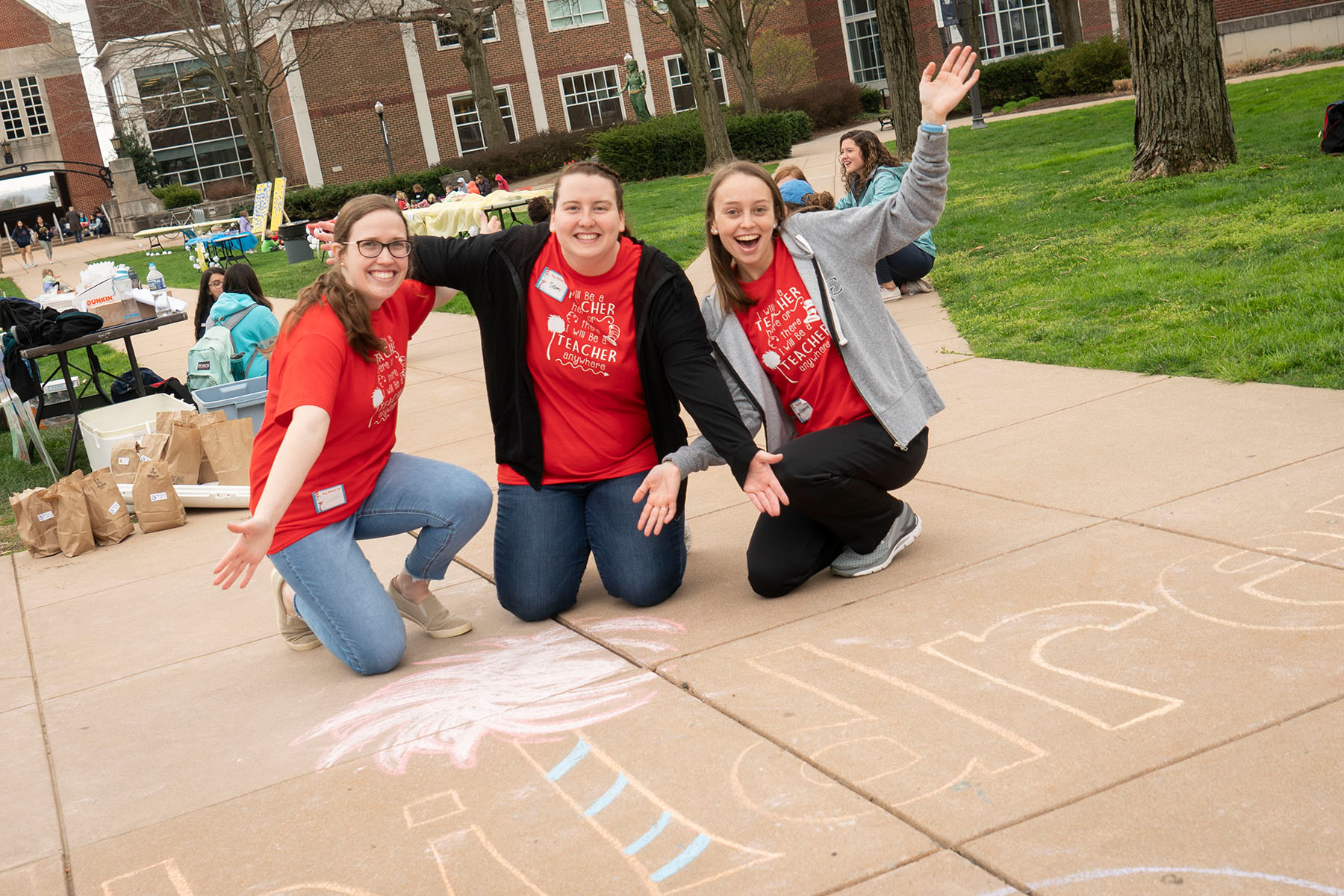 Student educators smiling by sidewalk chalk