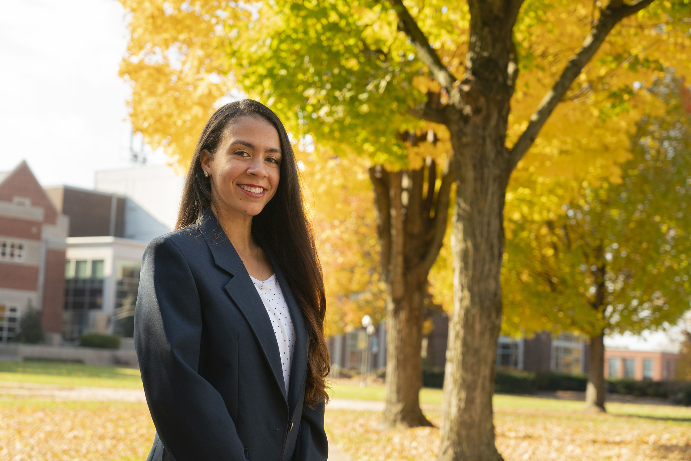 Female student in blazer smiling on autumn campus