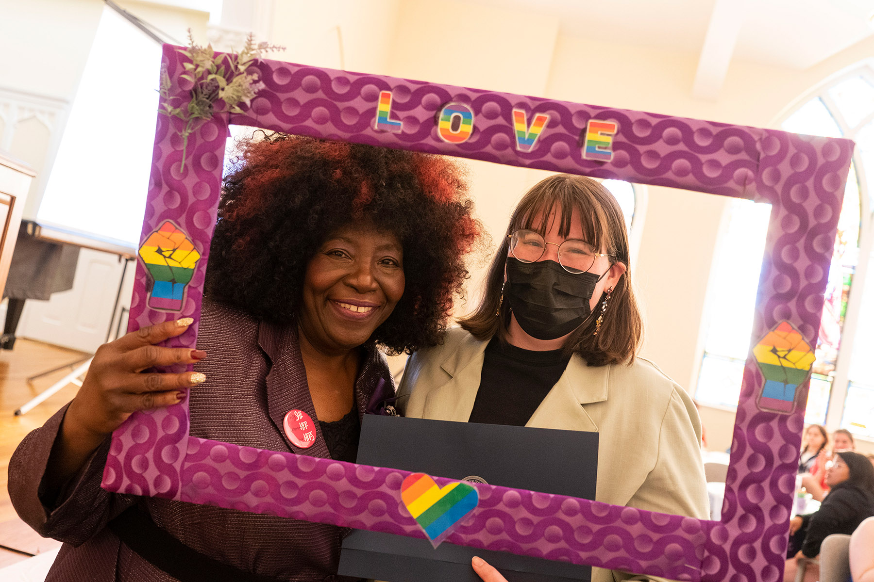Two women hold up photo frame with pride hearts