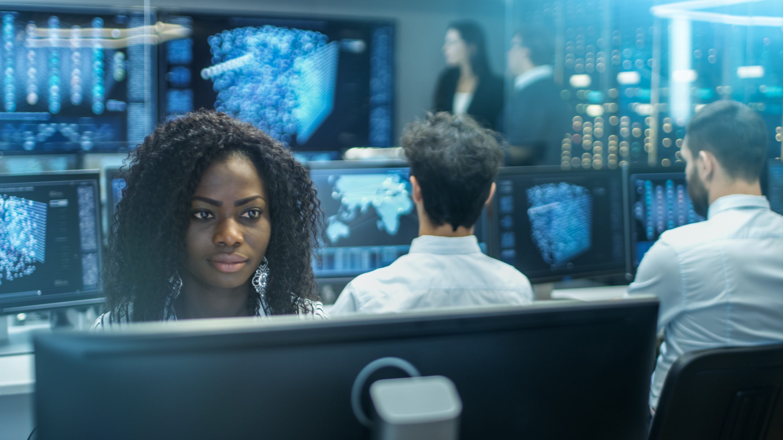 Female Computer Engineer Works on a Neural Network/ Artificial Intelligence Project with Her Multi-Ethnic Team of Specialist. Office Has Multiple Screens Showing 3D Visualization.