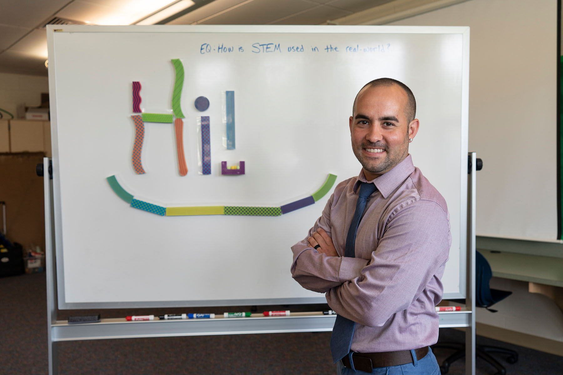 Teacher smiling in front of white board that says "hi!"
