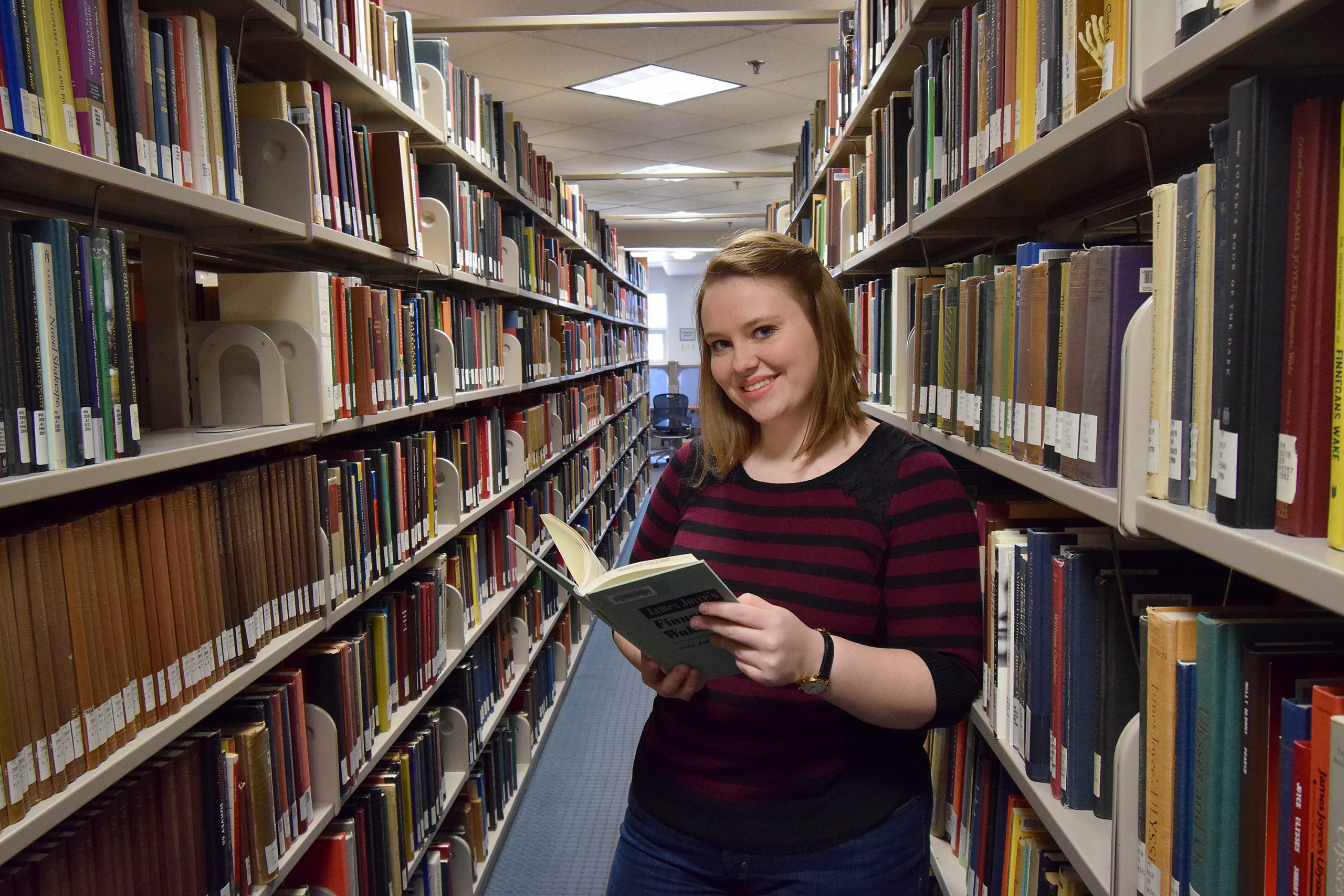 Student stands in row of books in library