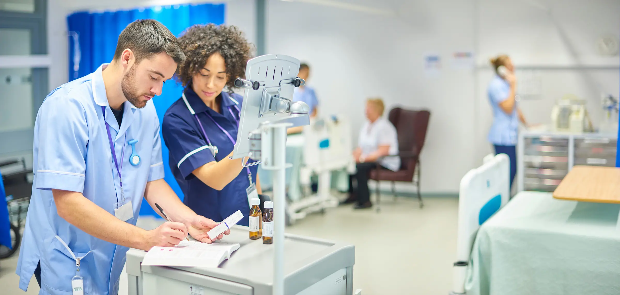 a male nurse checks the dosage on his digital tablet supervised by his staff nurse