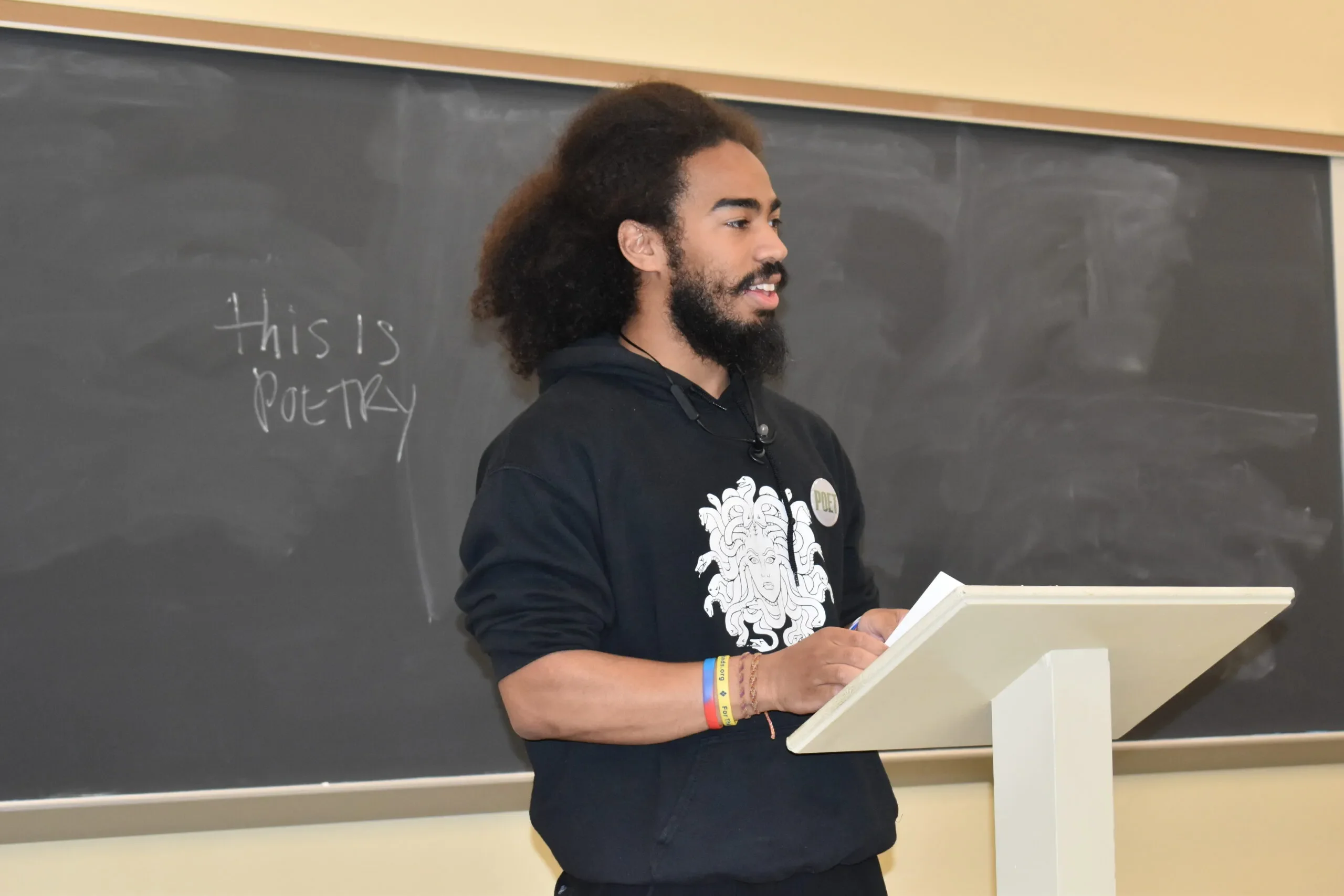 LVC English student Michai Figueroa stands at podium in front of chalkboard with the words, "This is poetry."