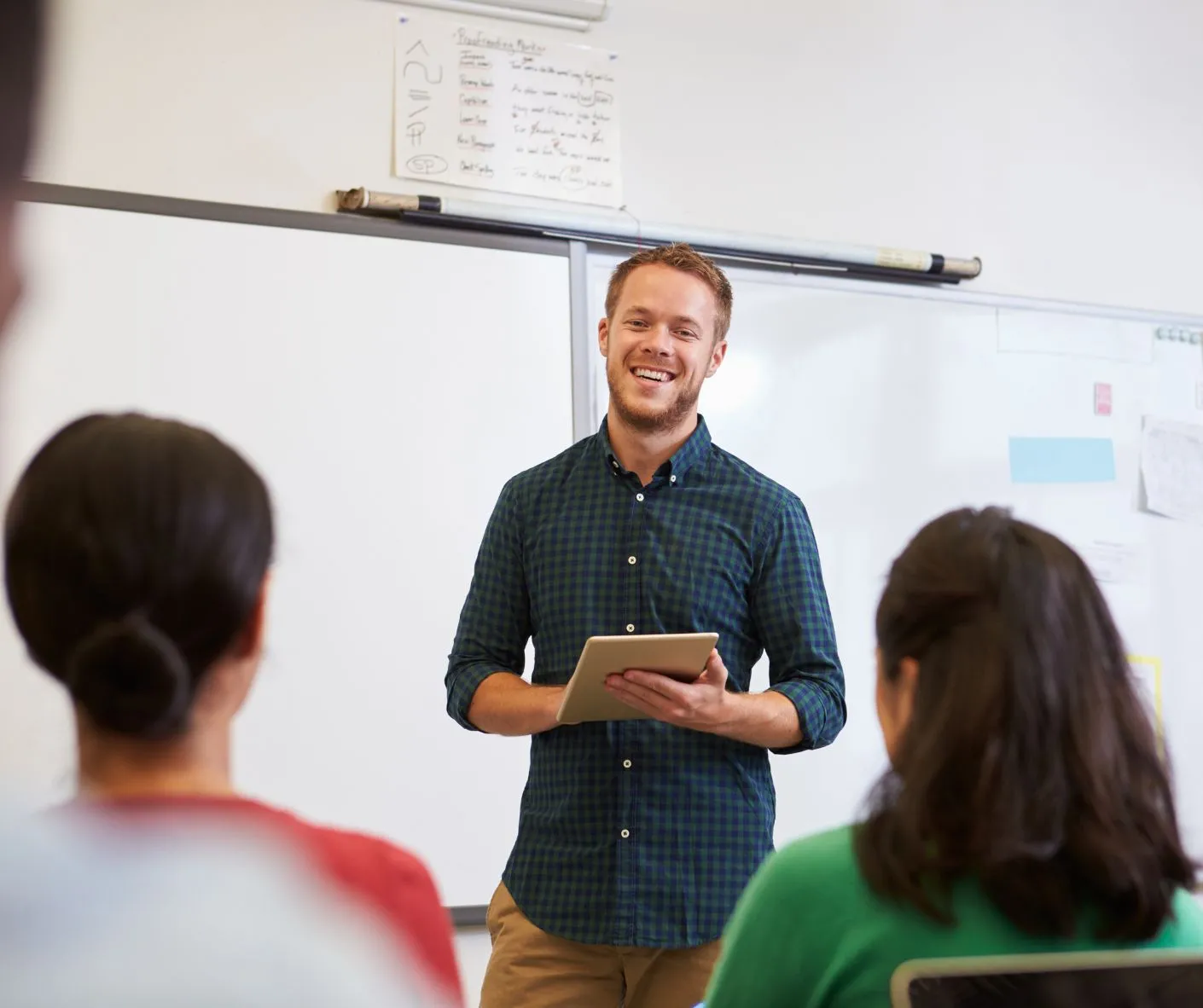 Teacher holds tablet in front of students in classroom