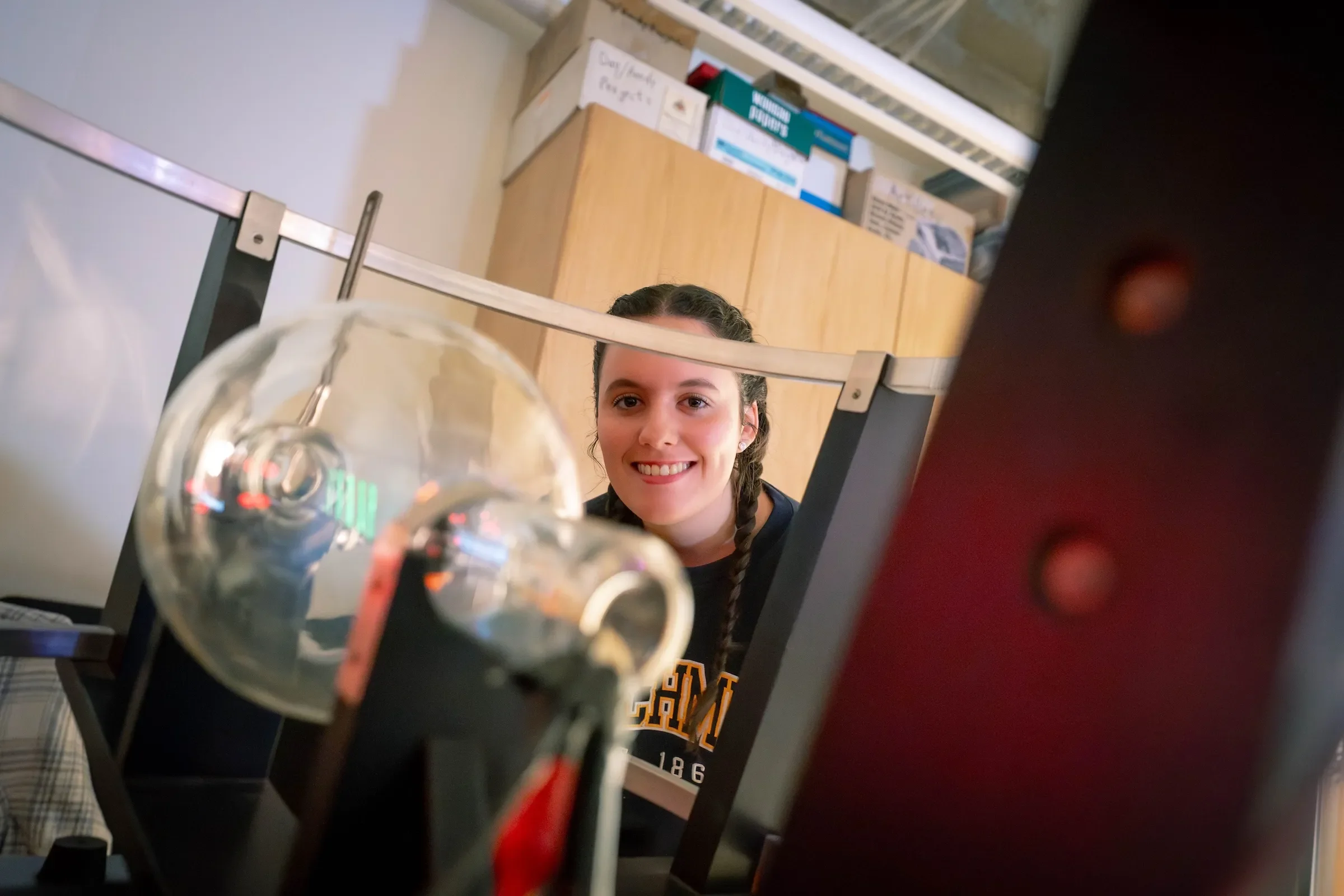 Student smiles from behind equipment in physics lab