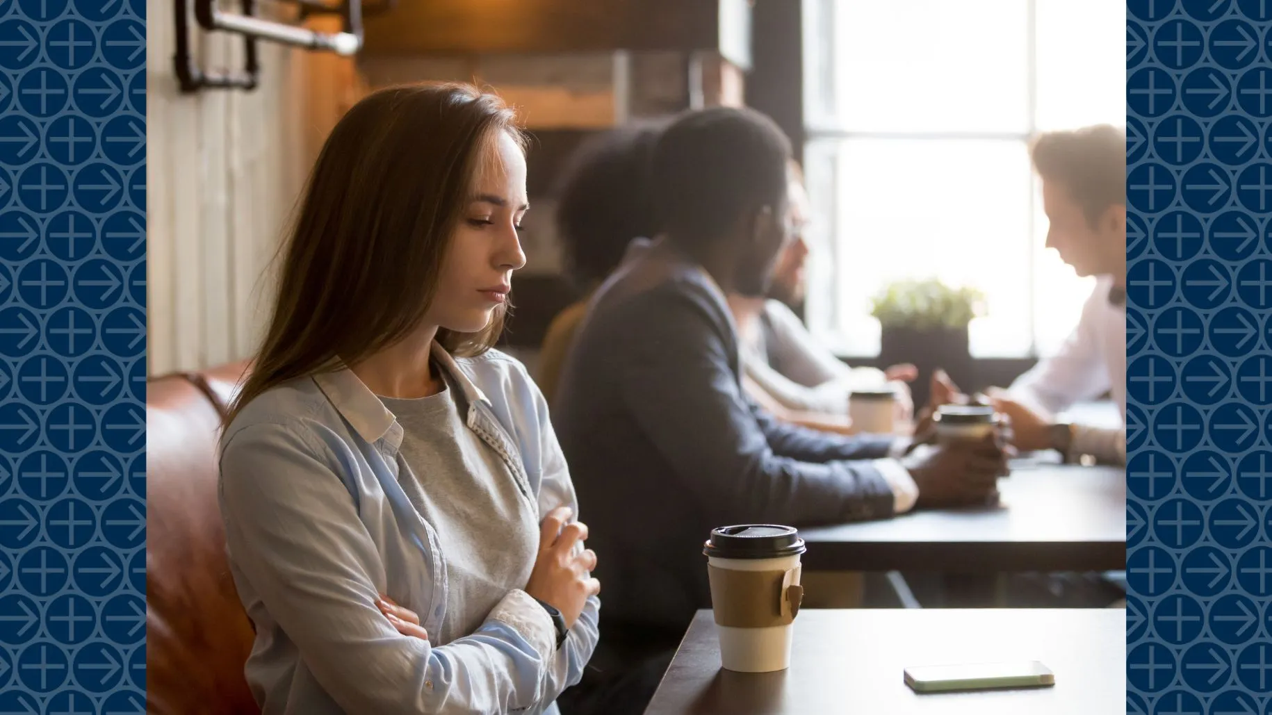 Young woman sits alone at cafe table next to group